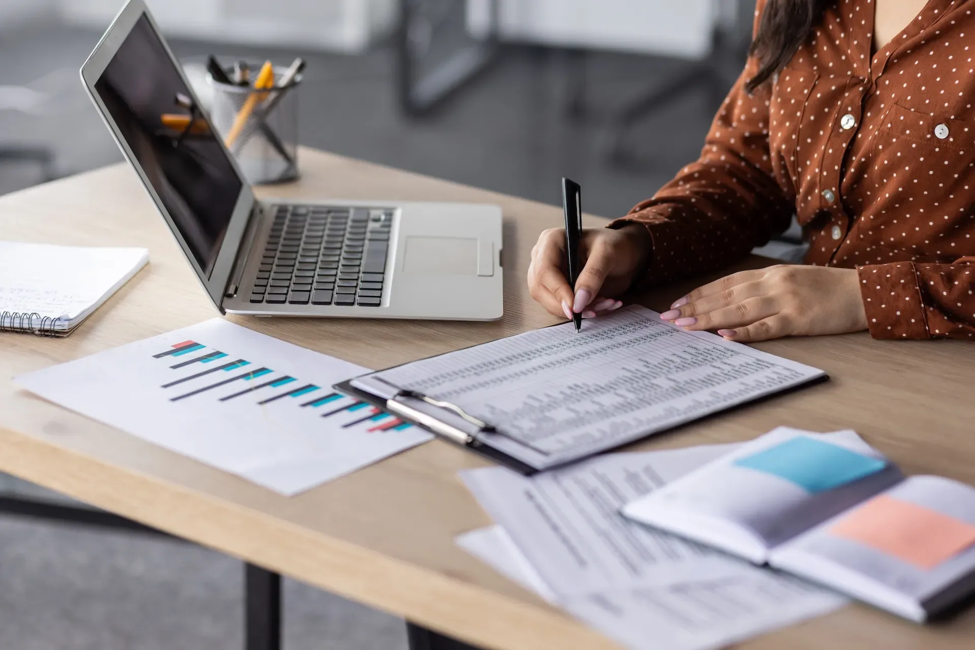 Bookkeeper reviewing financial reports and spreadsheets at a desk beside a laptop